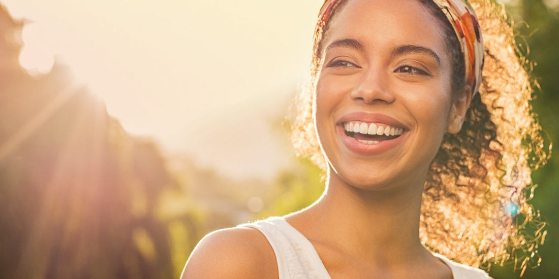 Women smiling with glowing skin, bright sun rays behind her